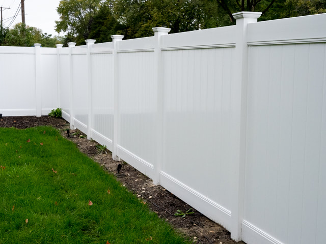 White vinyl privacy fence installed along a green lawn